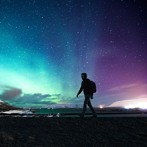 Solo traveller walking in front of the northern lights.