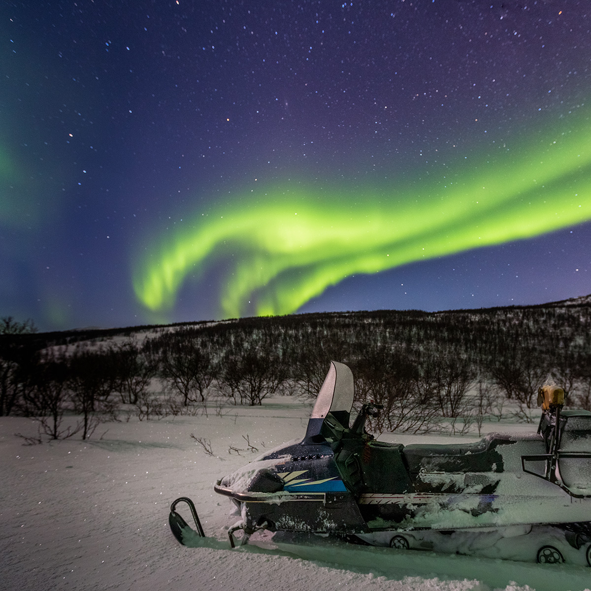 Green northern lights and snowmobile on foreground
